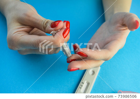 finger puncture to diagnose coronavirus. girl with red manicure makes herself an analysis on her own. girl holding a lancet and pricks her finger with the second hand, diagnostics at home finger puncture to diagnose coronavirus. girl with red manicure makes herself an analysis on her own. girl holding a lancet and pricks her finger with the second hand, diagnostics at home 73986506