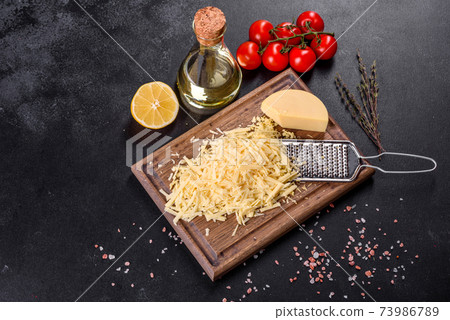 Fresh hard cheese grated on a large grater on a wooden cutting board 73986789