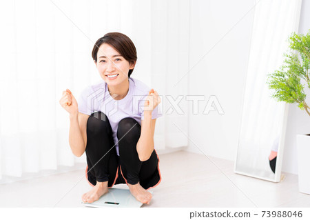 A middle-aged woman who rejoices on a scale after training at home 73988046