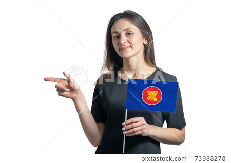 Happy young white woman holding flag Association of Southeast Asian Nations and points to the left isolated on a white background 73988278
