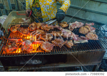 Woman grilling pork chop and ribs on flaming charcoal stove 73989392