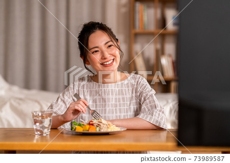 年輕女子在晚上吃飯時看電視 年輕女子在晚上吃飯時看電視 73989587
