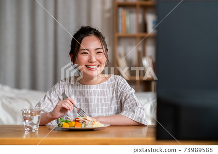 年輕女子在晚上吃飯時看電視 年輕女子在晚上吃飯時看電視 73989588