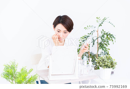 Middle-aged woman doing skin care while looking at her smartphone 73992169