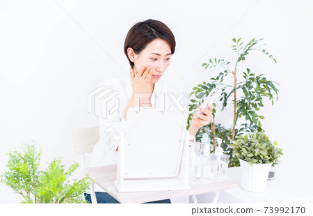 Middle-aged woman doing skin care while looking at her smartphone 73992170