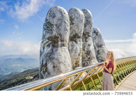 Young woman tourist at Famous tourist attraction - Golden bridge at the top of the Ba Na Hills, Vietnam Young woman tourist at Famous tourist attraction - Golden bridge at the top of the Ba Na Hills, Vietnam 73994655