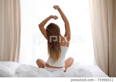 Woman stretching in bed after wake up, back view, entering a day happy and relaxed after good night sleep. Sweet dreams, good morning, new day, weekend, holidays concept 73996811