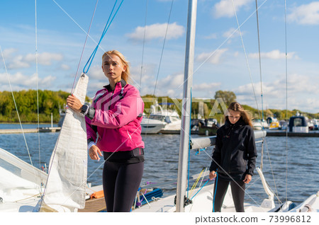 Two young blonde girls on a sunny summer day on a sailing boat are preparing for a river trip 73996812