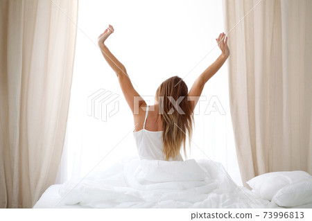 Woman stretching in bed after wake up, back view, entering a day happy and relaxed after good night sleep. Sweet dreams, good morning, new day, weekend, holidays concept 73996813