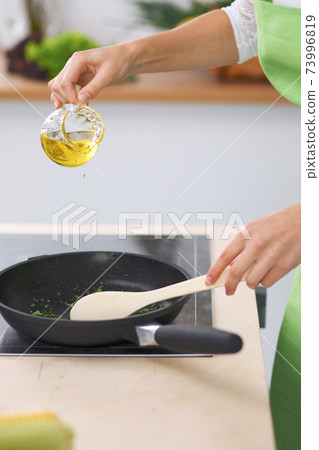 Young woman housewife cooking in the kitchen while adding olive oil. Concept of fresh and healthy meal at home 73996819