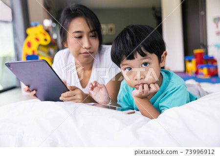 mother and her son using digital tablet in a bed at home. The use of concept of new generation, family, parenthood, authenticity, connection, technology. 73996912