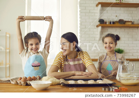 Mother and two daughters feeling excited during baking sweet bicsuits and making dough Mother and two daughters feeling excited during baking sweet bicsuits and making dough 73998267