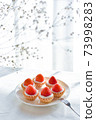 Small strawberry tart and haze grass lined up on a white plate 73998283