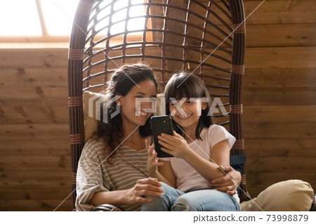 Close up mother with daughter using phone, sitting in armchair Close up mother with daughter using phone, sitting in armchair 73998879
