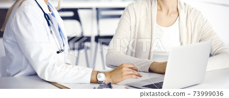 Unknown woman-doctor sitting and communicating with female patient. Physician checks medical history record and exam results, close-up. Healthcare concept Unknown woman-doctor sitting and communicating with female patient. Physician checks medical history record and exam results, close-up. Healthcare concept 73999036