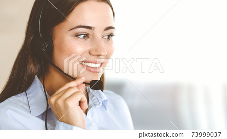 Brunette female customer service representative using headset and consulting clients online. Call center 73999037