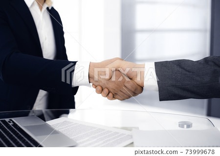 Unknown diverse business people are shaking hands finishing up meeting at the desk in office, close-up. Handshake concept Unknown diverse business people are shaking hands finishing up meeting at the desk in office, close-up. Handshake concept 73999678