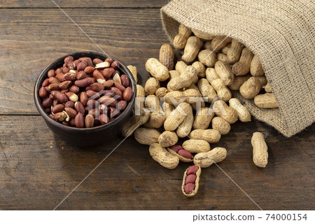 Peanuts in shell and peeled peanuts in a bowl on a wooden table. Beer snacks. Healthy food concept. Peanuts in shell and peeled peanuts in a bowl on a wooden table. Beer snacks. Healthy food concept. 74000154