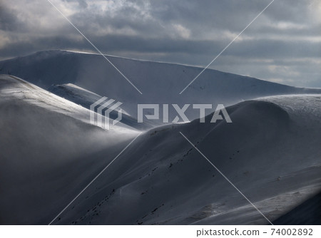 Snow covered winter mountains  in last evening sunlight. Magnificent windy dusk. 74002892