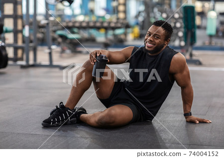 Happy black bodybuilder with water sitting on floor 74004152