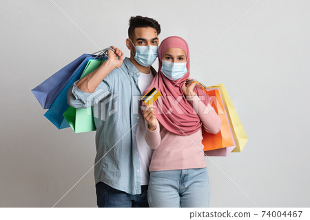 Happy muslim couple wearing masks holding credit card and paper shopping bags Happy muslim couple wearing masks holding credit card and paper shopping bags 74004467