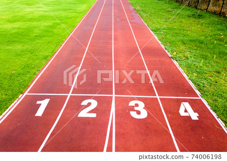 Aerial view of sports stadium with red running tracks with numbers on it and green grass football field. 74006198