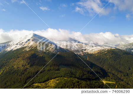Aerial view of majestic mountains covered with green spruce forest and high snowy peaks. Aerial view of majestic mountains covered with green spruce forest and high snowy peaks. 74006290
