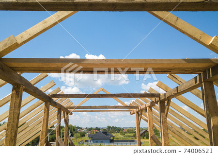 Aerial view of unfinished house with wooden roof frame structure under construction. 74006521