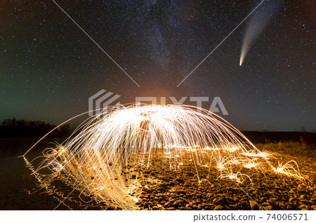 Long exposure of spinning steel wool in abstract circle making firework showers of yellow glowing sparks with dark night starry sky above. Long exposure of spinning steel wool in abstract circle making firework showers of yellow glowing sparks with dark night starry sky above. 74006571