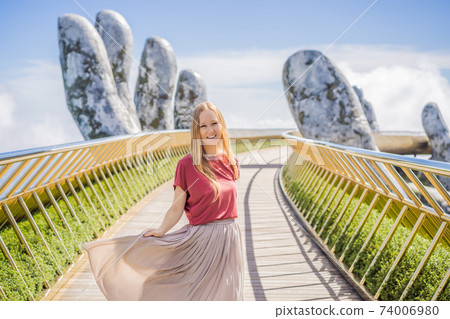 Young woman tourist at Famous tourist attraction - Golden bridge at the top of the Ba Na Hills, Vietnam Young woman tourist at Famous tourist attraction - Golden bridge at the top of the Ba Na Hills, Vietnam 74006980