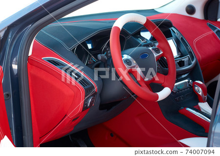 Steering wheel. Car dashboard. Car interior details. Red and black alcantara with stitching 74007094