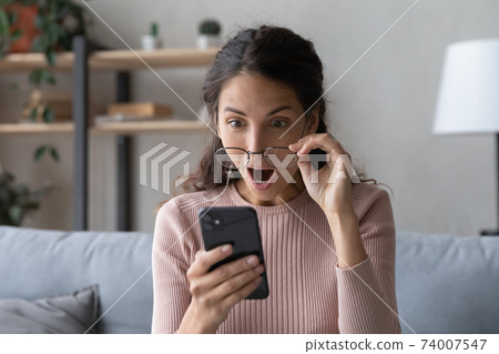 Emotional young woman looking at smartphone screen with opened mouth. 74007547