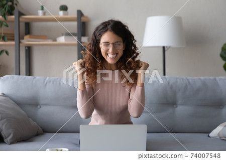 Overjoyed young woman in eyeglasses celebrating online lottery win. 74007548