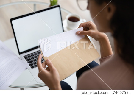 Close up young woman opening envelope with letter. 74007553