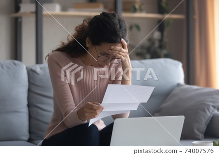 Stressed young caucasian woman reading paper with bad news. 74007576