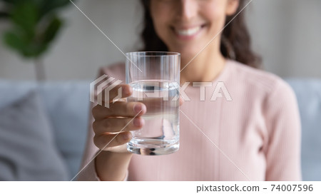 Close up glass with mineral clean water in female hands. Close up glass with mineral clean water in female hands. 74007596