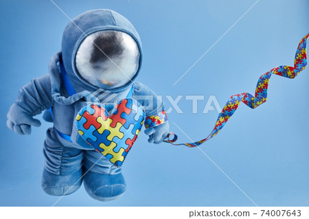 World Autism awareness day background. Blue plush astronaut toy with puzzle heart, autism symbol, on blue background 74007643