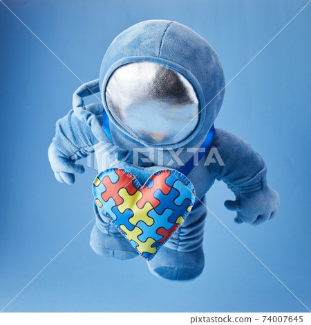 World Autism awareness day background. Blue plush astronaut toy with puzzle heart, autism symbol, on blue background 74007645