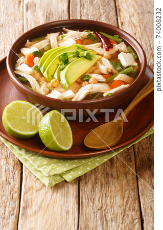 Mexican caldo tlalpeno soup, made with homemade chicken stock, a chipotle tomato base, and shredded chicken closeup on the table. Vertical 74008232