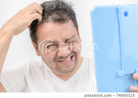A middle-aged man shines in the mirror and uses his hands to scratch his hair on the scalp.Itchy head A middle-aged man shines in the mirror and uses his hands to scratch his hair on the scalp.Itchy head 74008328