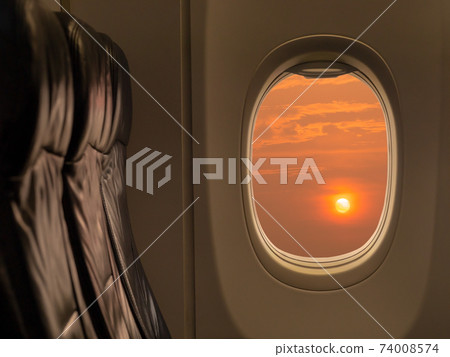 Big sun at sunset sky from airplane window. Travelling by airplane seat near window enjoying beautiful sunset. Sunset through aircraft window. 74008574