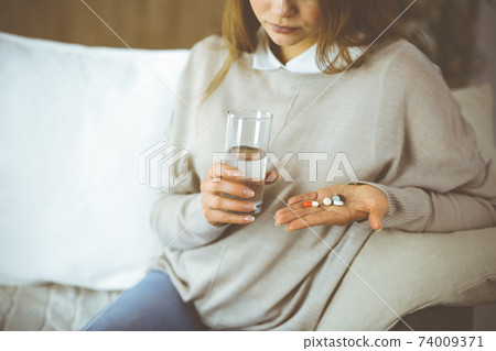Close-up woman holding pills time to take medications, cure for headache, high blood pressure pain killer drugs at home. Stay at home concept during Coronavirus pandemic Close-up woman holding pills time to take medications, cure for headache, high blood pressure pain killer drugs at home. Stay at home concept during Coronavirus pandemic 74009371
