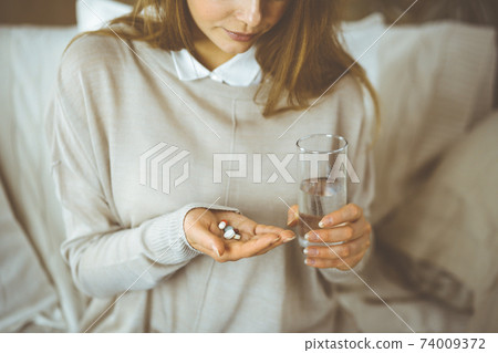 Close-up woman holding pills time to take medications, cure for headache, high blood pressure pain killer drugs at home. Stay at home concept during Coronavirus pandemic 74009372