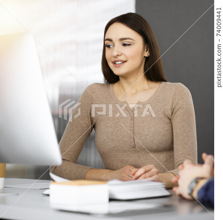 Young business people are talking to each other, while sitting at the desk in sunny office. Businesswoman is explaining something to her colleague Young business people are talking to each other, while sitting at the desk in sunny office. Businesswoman is explaining something to her colleague 74009441
