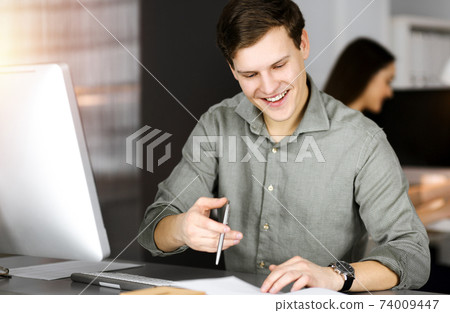 Young businessman working on his computer sitting at the desk in office. Headshot portrait of a man Young businessman working on his computer sitting at the desk in office. Headshot portrait of a man 74009447