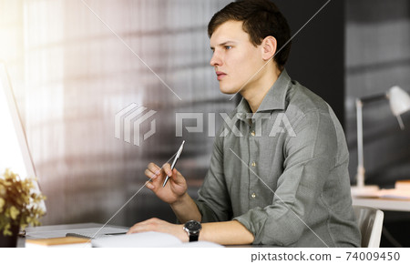 Young businessman working on his computer sitting at the desk in office. Headshot portrait of a man 74009450