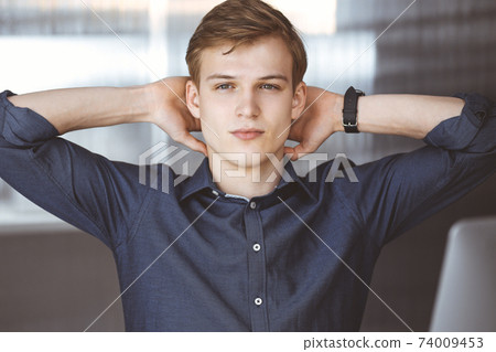 Happy blond businessman and programmer stretching hands after working hard with computer. Startup business leads to success Happy blond businessman and programmer stretching hands after working hard with computer. Startup business leads to success 74009453
