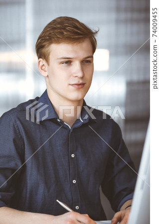 Young blond businessman working with computer. Startup business means working hard and out of time for success achievement Young blond businessman working with computer. Startup business means working hard and out of time for success achievement 74009455