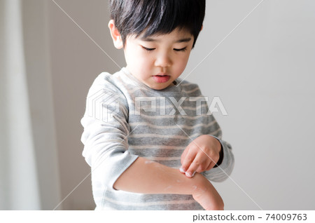 Boys applying moisturizing cream to dry skin 74009763