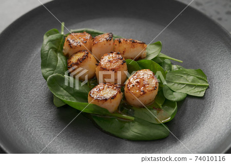 Seared scallops on pile of spinach on black plate closeup 74010116